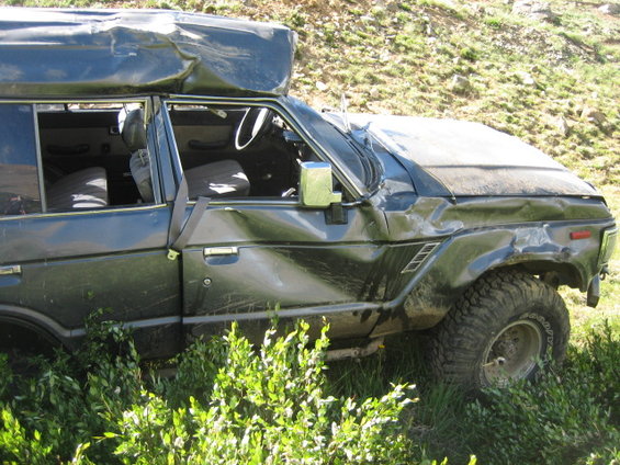 Damaged dark SUV side view with dented doors and hood