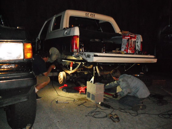 Rear view of lifted SUV with "UC 4X4" on the tailgate, being worked on by two people