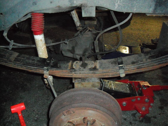 Rear leaf spring, shock absorber, brake drum, and red hydraulic jack under a vehicle