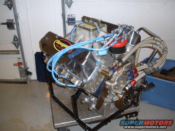 V8 engine with chrome valve covers and blue spark plug wires, mounted on a metal stand