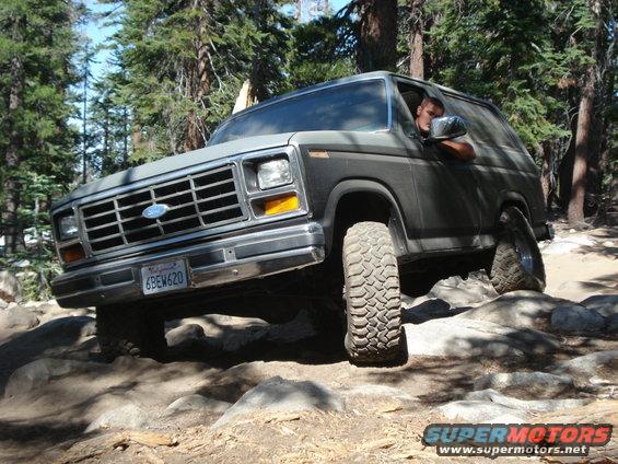 Ford Bronco navigating rocky terrain on a wooded trail. License plate reads 6BEW620