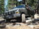 1984 Ford Bronco - This Ford Bronco is tackling a challenging off-road course with large rocks and trees surrounding it.