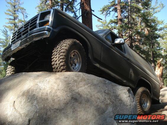 Dark SUV with off-road tires on a large rock, front grille visible