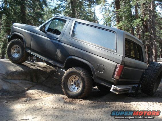 Gray 1984 Ford Bronco off-roading on rocks, 3/4 front view