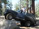 1984 Ford Bronco - A man stands in the open door of a dark SUV as it navigates a rocky trail.
