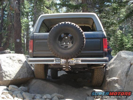 Rear view of dark SUV with spare tire, off-roading over rocks
