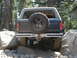 1984 Ford Bronco - This dark SUV is seen from the rear, maneuvering over a rocky trail with its spare tire mounted externally.