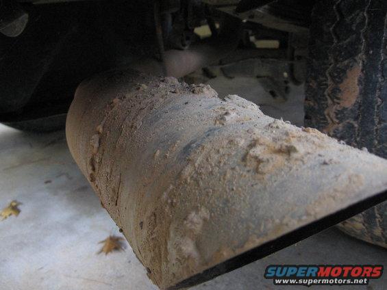 Close-up of a dirty exhaust pipe with a tire in the background