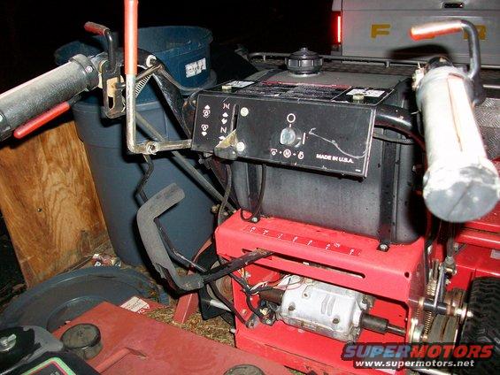 lawnmower engine with controls, gas tank, and part of a truck in background