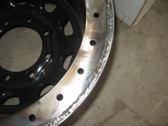 Close-up of a black steel wheel rim with a welded silver outer lip and multiple bolt holes