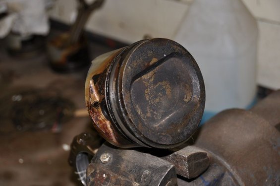 Close-up of a heavily used piston held in a vise, showing signs of wear and carbon buildup