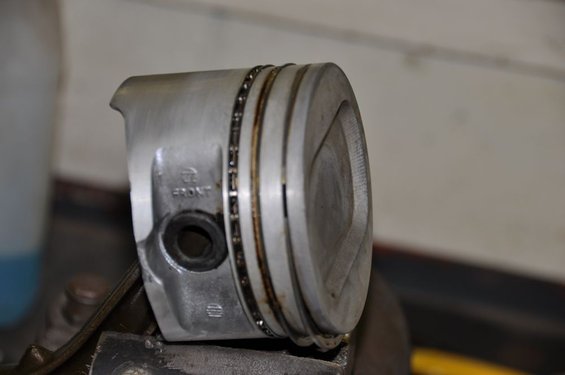 Piston with oil rings, marked 'FRONT', held in a vise