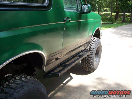 Green SUV, looks like a Ford Bronco, with big off-road tires and black side steps. It's parked on a driveway