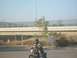 1985 Honda CMX250 Rebel - A person rides a motorcycle on a road with a highway overpass in the background.