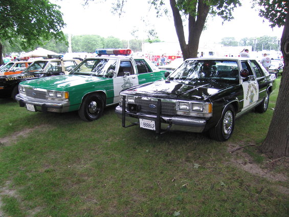 1991 Ford Crown Victoria police car and a green police car parked on grass