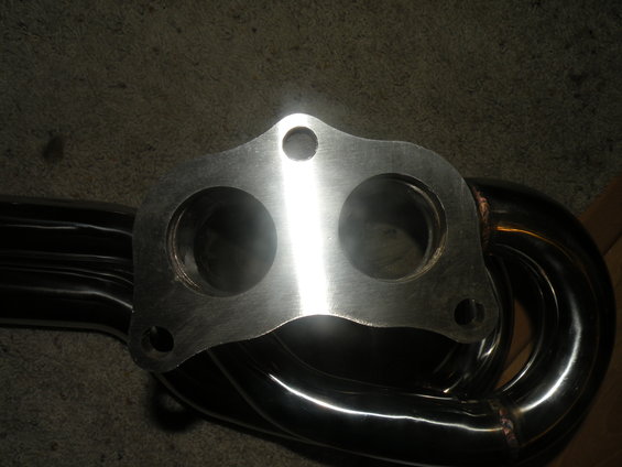 Close-up of a polished metal exhaust manifold with two large circular openings and three smaller bolt holes