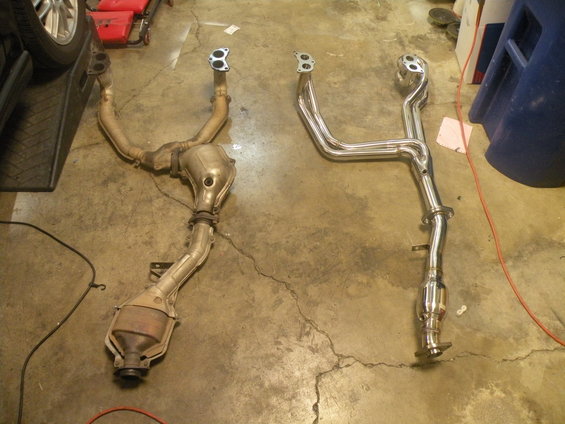 Two exhaust systems, one old and rusty, one new and shiny, laid out on a concrete floor