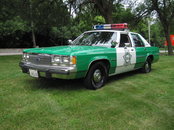 Green and white 1991 Ford Crown Victoria police car parked on grass, front 3/4 view