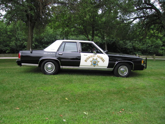 Side view of a black and white 1991 Ford Crown Victoria highway patrol car parked on grass