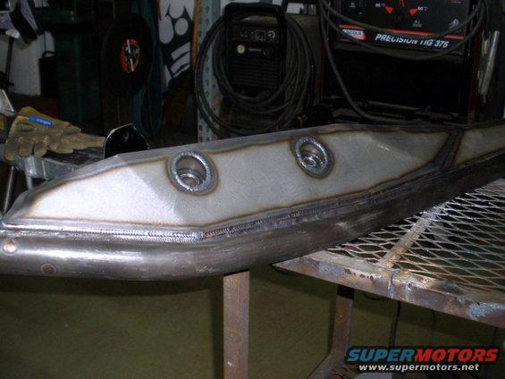 welded metal component with two circular openings, resting on a metal grate