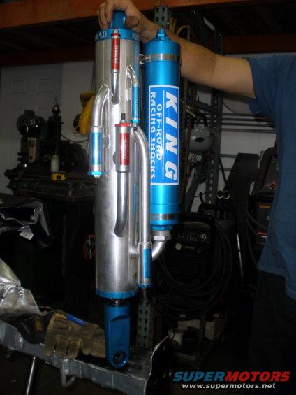 Two King Off-Road Racing Shocks, one silver and one blue, held by a person in a workshop