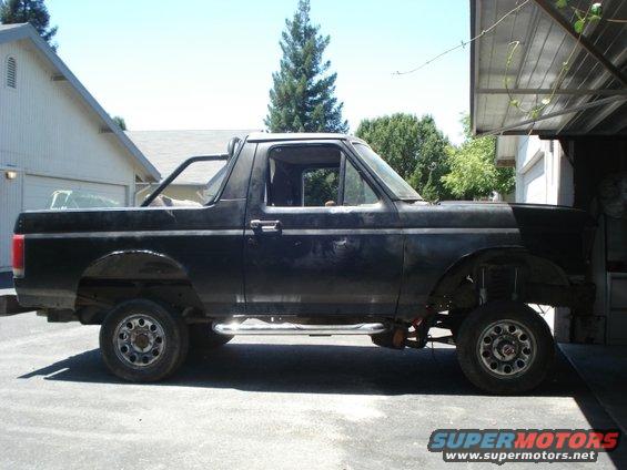 Black Ford Bronco with a roll bar, parked outside a garage. It looks like it's undergoing some work