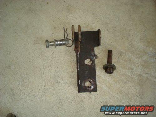 metal bracket with a pin and spring, plus a separate bolt, lying on a concrete surface