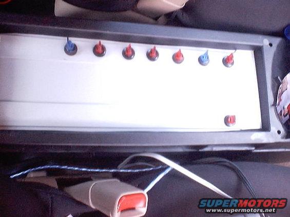 Interior panel with several red and blue switches, seatbelt buckle visible