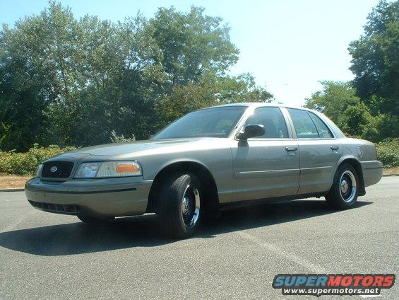 Tan 2000 Ford Crown Victoria sedan parked on asphalt, front three-quarter view, trees in background