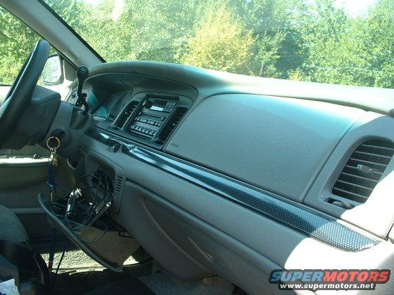 Dashboard of a 2000 Ford Crown Victoria, showing the steering wheel, radio, air vents, and open glove compartment with wires