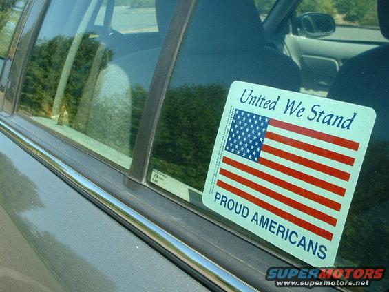 Gray car interior, side window with American flag sticker reading "United We Stand Proud Americans"