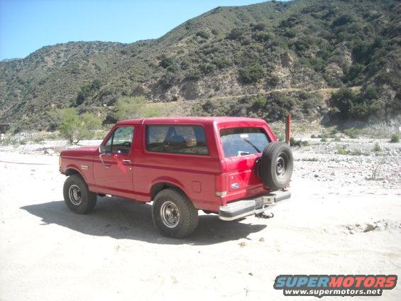 Red 1988 Ford Bronco parked in a dry riverbed, rear quarter view with spare tire mounted