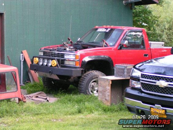 red pickup truck, hood open, custom bumper with smiley face lights, parked next to a black truck
