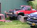 1984 Chevrolet Blazer - A red pickup truck with its hood up is parked next to a black truck, with a wooden crate on a stand between them.