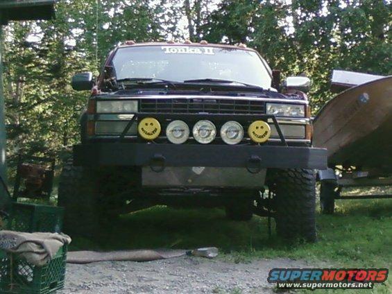 Front view of a lifted pickup truck with a custom bumper and smiley face lights. "Tonka II" sticker on windshield