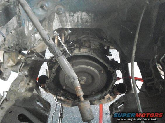 Underside view of a vehicle's transmission and driveshaft assembly, appears to be undergoing maintenance or disassembly