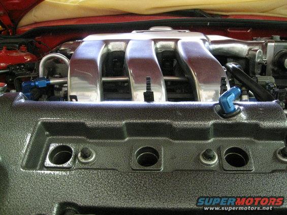 Engine intake manifold with chrome runners and textured grey valve cover. Blue spark plug wire boot visible