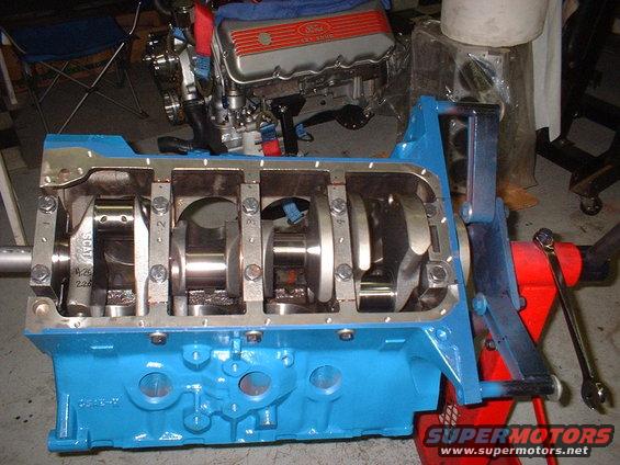 Blue engine block with crankshaft and SCAT connecting rods visible. Ford valve cover in background