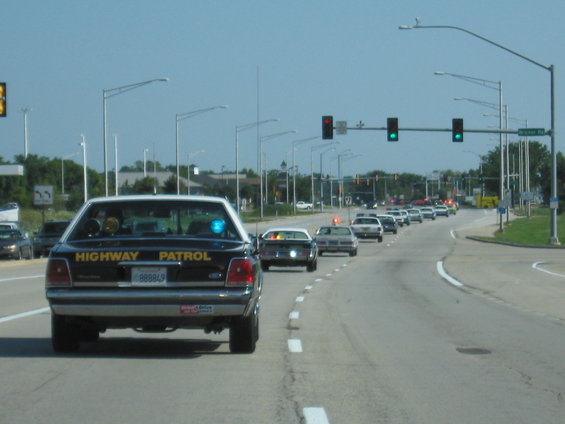 Highway Patrol car leading a line of cars on a sunny day