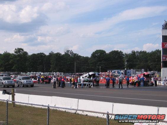 Silver SUVs and race cars on a track with spectators and RVs