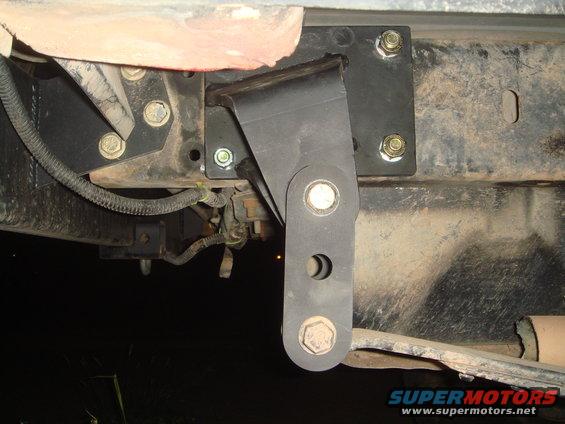 close-up of a black metal bracket bolted to a vehicle frame, with a dangling piece and bolts