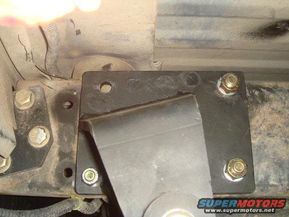 Aftermarket suspension bracket bolted to vehicle frame, showing metal plates and bolts