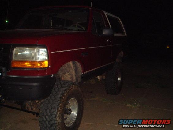 Red SUV with large tires parked at night. Side profile shows front fender and door