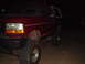 1992 Ford Bronco - This red SUV is parked outside at night, showing off its large tires and lifted suspension.
