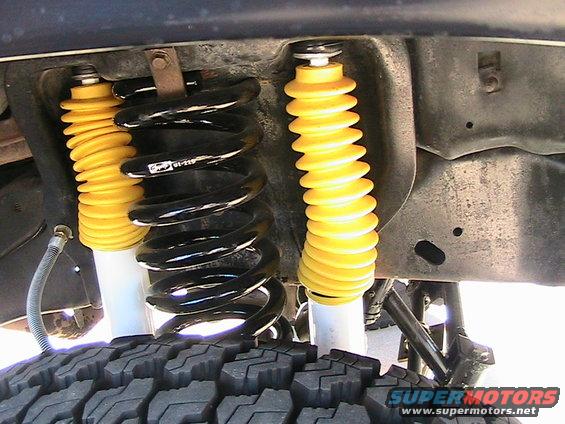 Close-up of front suspension with yellow shock boots and black coil springs