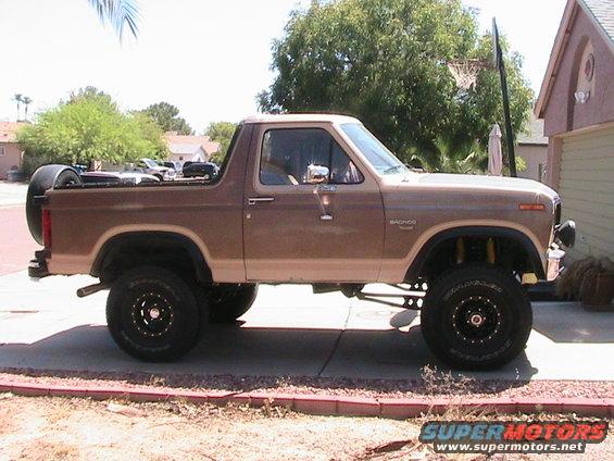 Brown two-tone Ford Bronco with lifted suspension and spare tire on the back, parked on a driveway