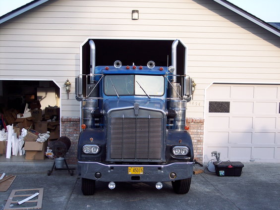 Blue 1981 Kenworth W900A semi-truck parked in front of a garage, front view