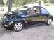1999 Volkswagen Beetle - A black Volkswagen Beetle is parked outdoors on a dirt surface with trees in the background.