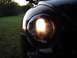 1999 Volkswagen Beetle - Close-up of a 1999 Volkswagen Beetle's illuminated headlight against a grassy background.