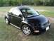 1999 Volkswagen Beetle - A black Volkswagen Beetle is parked on a grassy area with trees in the background.